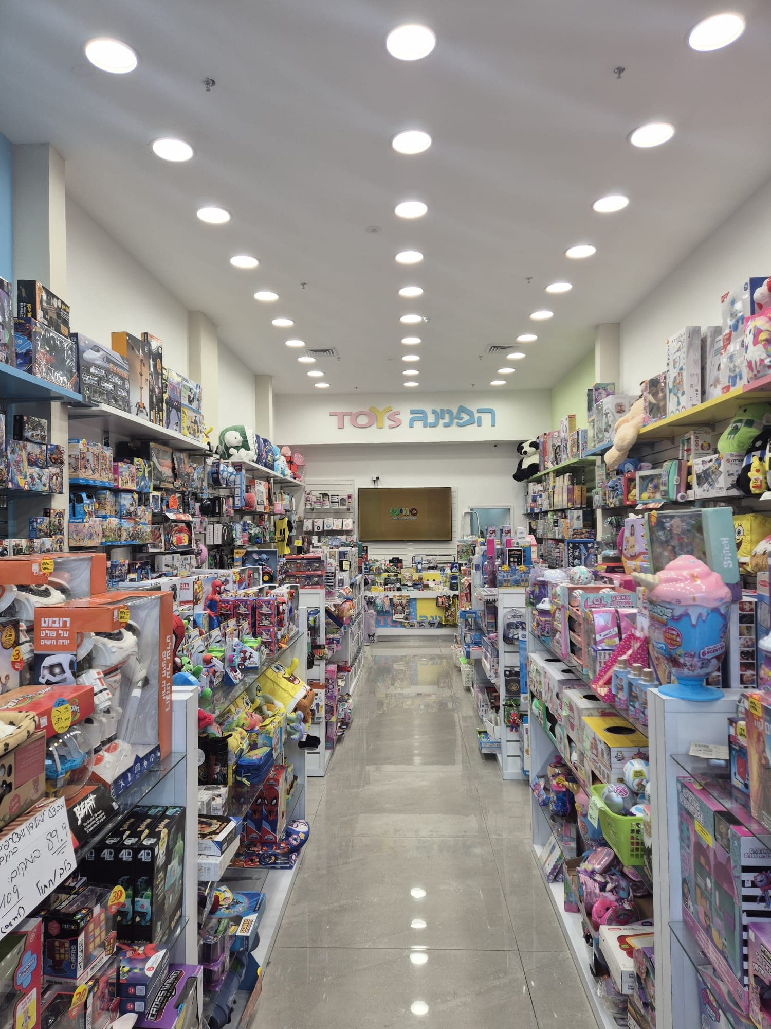 פנים חנות הצעצועים "הפנינג TOYS" עם מדפים רבים המציגים מגוון רחב של משחקים ובובות.