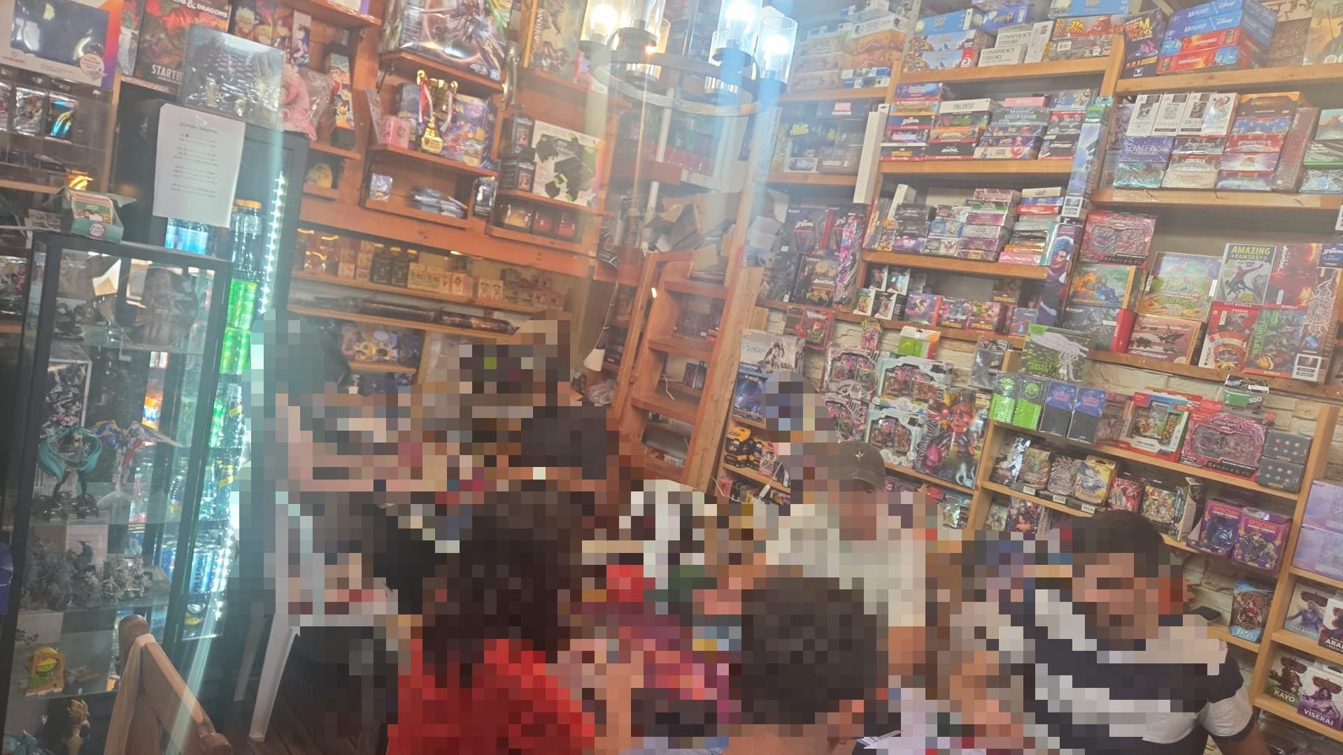 שחקנים משתתפים בטורניר משחקי קלפים בחנות סירולניה בירושלים, מוקפים במבחר משחקים ואספנות.