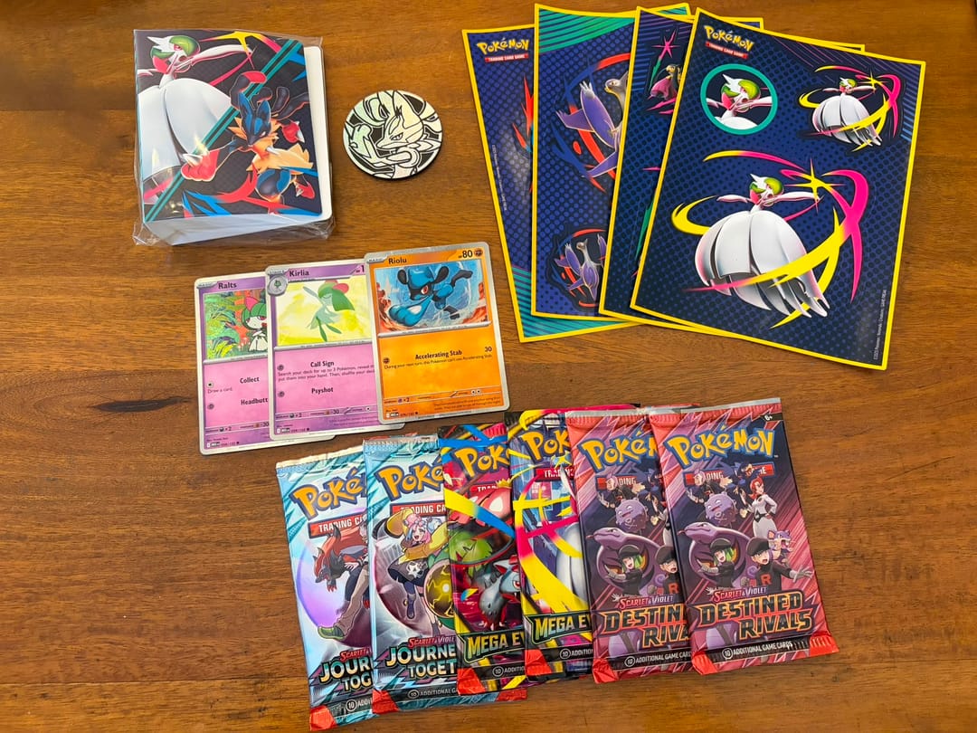 תכולת מארז Pokémon TCG Collector Chest: קופסת פח עם מגה גארדוויר ומגה לוקאריו, מטבע לוקאריו, דפי מדבקות ו-3 קלפי פרומו (Ralts, Kirlia, Riolu). כמו כן מוצגות 6 חבילות בוסטר מהסטים Journey Together, Mega Evolution ו-Destined Rivals.